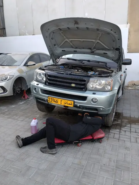 A technician under a Range Rover Sport with the bonnet open